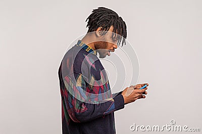 Extremely surprised african man with dreadlocks widely open his mouth holding mobile phone, wondered shocked with bonuses Stock Photo