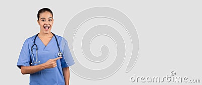 An exuberant female doctor in blue scrubs enthusiastically points to her left with a wide smile Stock Photo