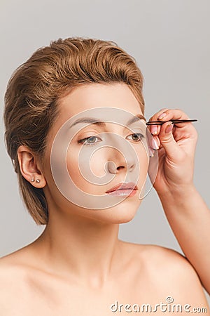 Eyebrow correction with tweezers, blonde model face with makeup nude. Close-up shot in the studio Stock Photo