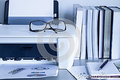 Eyeglasses on printer with books on wooden table Stock Photo