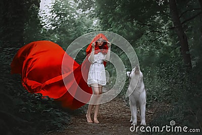 Fabulous girl with dark hair in short light white dress covers her head with hood of long bright red flying fluttering Stock Photo