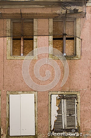 Facade of abandoned, dilapidated house with 4 boarded windows, shutters, boards and flow as protection from falling tiles and Stock Photo