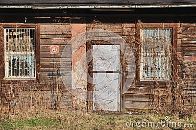 Facade of an abandoned wooden old house with dilapidated door and rusty windows with bars Stock Photo