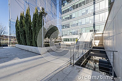 Facade of an office building with marble stairs with metal railings and decorative trees Stock Photo