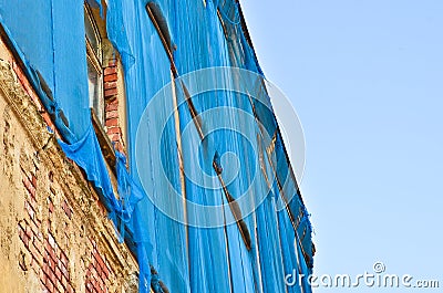 The facade of an old ruinous building is mantled with some blue curtains to protect the pedestrians Stock Photo