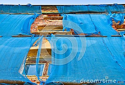 The facade of an old ruinous building is mantled with some blue curtains to protect the pedestrians Stock Photo