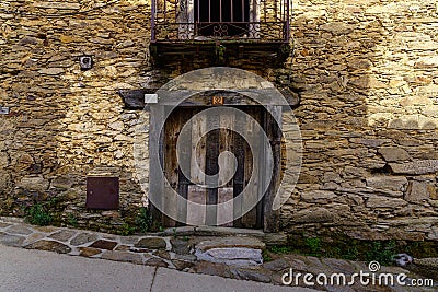 Facade of a very old house with a wooden door and a balcony with iron bars. La Hiruela Madrid Stock Photo