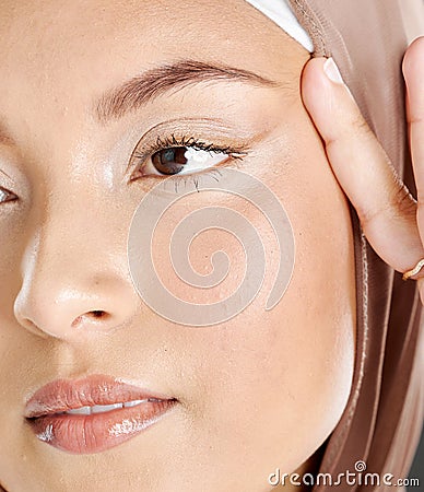 Face of a beautiful Muslim woman wearing a brown headscarf and lifting the skin around her eyes. Headshot of hijab lady Stock Photo