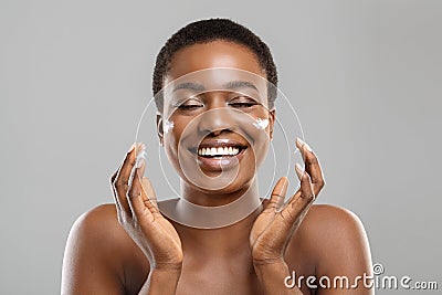 Beautiful afro woman applying cream on her cheeks and sincerely smiling Stock Photo