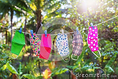 Face masks with different style prints hang and dry on clothespins outdoors at sunset Stock Photo