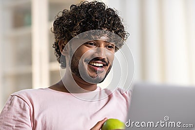 A face of positive smiling mestizo guy in joyful and happy mood. A young charming african or american man eats apple Stock Photo