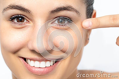 Face shot of attractive young woman pointing with finger at crow`s feet on face Stock Photo