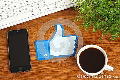 Facebook thumbs up sign placed on wooden background with coffee, keyboard and smart phone Editorial Stock Photo