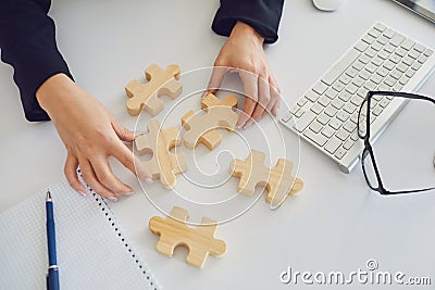 Faceless hands of a businesswoman with wooden puzzles on a white table in the office. Stock Photo