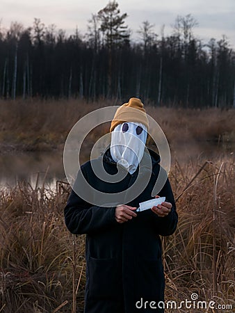 Faceless killer. Dangerous man with a white cloth on his face and a knife in his hand on the reeds in the evening. Halloween Stock Photo