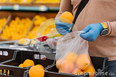 Faceless man buyer chooses fresh oranges in shopping mall, afraids of coronavirus, wears rubber gloves during virus outbreak, buys Stock Photo