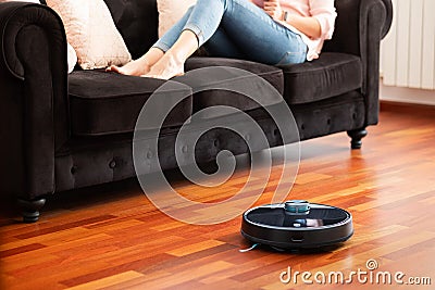 Faceless middle section of young woman relaxing on coach using automatic vacuum cleaner to clean the floor Stock Photo