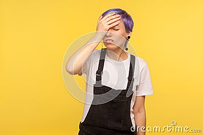 Facepalm. Portrait of forgetful hipster girl holding hand on forehead. yellow background, studio shot Stock Photo