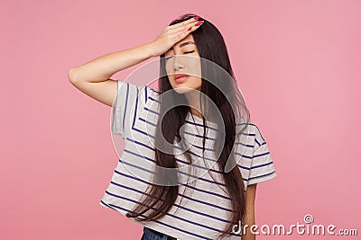 Facepalm. Portrait of regretful girl with brunette hair in striped t-shirt slapping hand on forehead, feeling sorrow Stock Photo