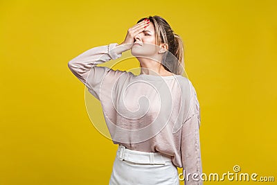 Facepalm. Portrait of regretful young woman with fair hair in casual beige blouse, isolated on yellow background Stock Photo