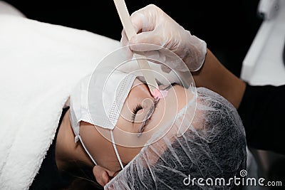 Facial hair removal procedure by hot wax on wooden stick, preparation before permanent makeup tattoo on eyebrows. Stock Photo