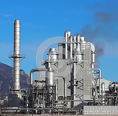 Factory with a long metal chimney and many pipes around an industrial building Stock Photo