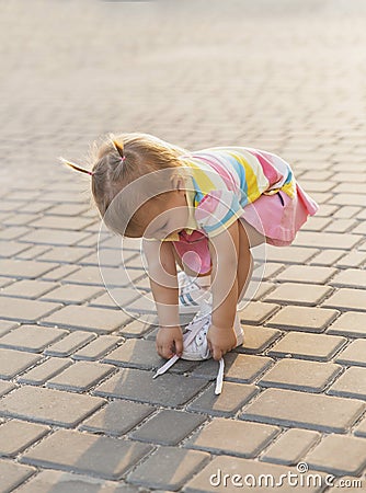 Fair-haired baby in tennis clothes ties shoelaces at sunset Stock Photo