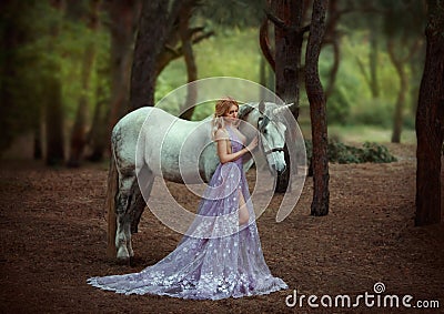 A fairy in a purple, transparent dress with a long train - caught a unicorn. Fantastic magical, radiant horse. Blonde Stock Photo