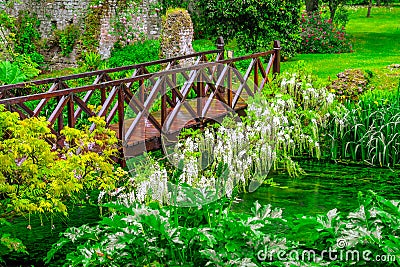Fairy tale bridge vivid green river wooden full of flowers in ornamental garden Stock Photo