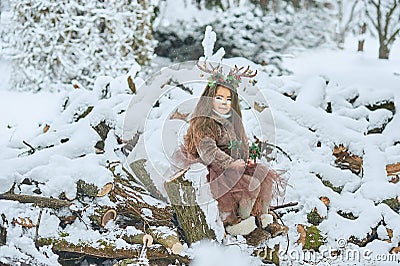 Fairy tale girl. Portrait a little girl in a deer dress with a painted face in the winter forest. Big brown antler Stock Photo