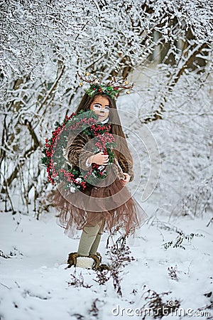 Fairy tale girl. Portrait a little girl in a deer dress with a painted face in the winter forest. Big brown antler Stock Photo