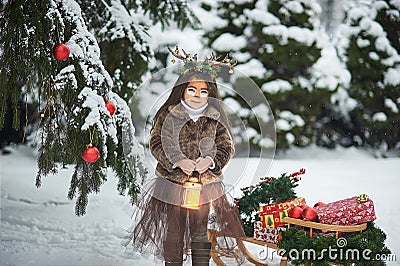 Fairy tale girl. Portrait a little girl in a deer dress with a painted face in the winter forest. Big brown antler Stock Photo