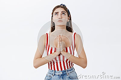 Faithful adult woman in striped top and headband holding palms in pray against chest raising head up looking in sky Stock Photo