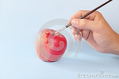 Fake food, coloring, fraud and fraudulent food concept. Hand painting an apple with artificial red colorant or paint. Stock Photo