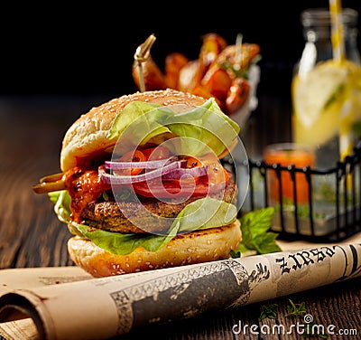 Falafel burger with addition of lettuce, tomato, onion, pickle cucumbers, spicy aromatic sauce and herbs on a wooden rustic table. Stock Photo