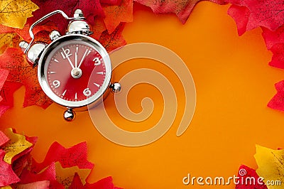 Fall back, the end of daylight savings time and turn clocks back on hour concept with a clock surrounded by dried yellow leaves Stock Photo