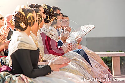 Falleras in a public event sitting clapping. Hairstyle and dress typical of the parties of the Fallas of Valencia Editorial Stock Photo