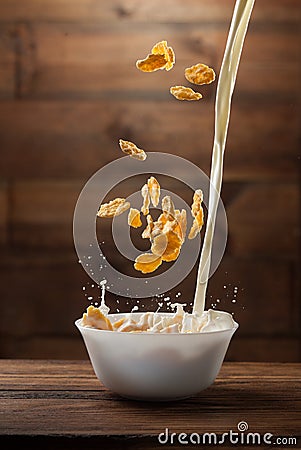 Falling corn flakes with milk splash on wood Stock Photo