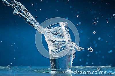Falling small glasses and spilling water on a blue background Stock Photo