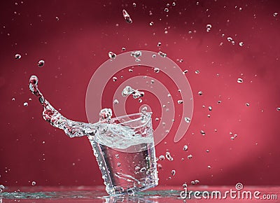 Falling small glasses and spilling water on a blue background Stock Photo