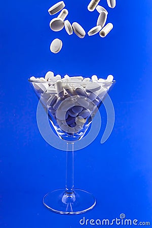 Falling white pills, tablets capsule in a martini glass on blue backround. Anti gravity concept Stock Photo