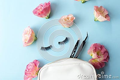 False eye lashes, black tweezers and pink flowers on blue background. Beauty concept - Tools for eyelash extension Stock Photo