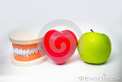 False teeth denture against green granny smith apple. Dental prosthesis care. Denture and Apple in the hands of a doctor. Food and Stock Photo