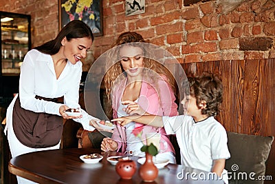 Family At Cafe. Waitress Serving Chocolate To Mother And Son Stock Photo