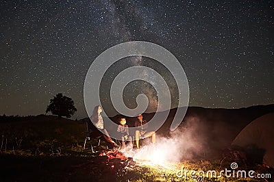 Family beside camp, campfire, tent under night starry sky Stock Photo