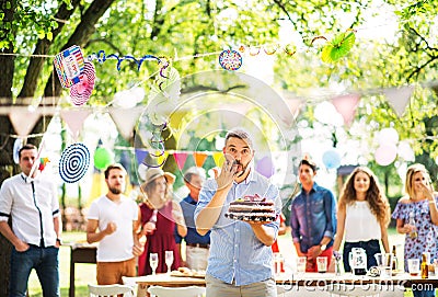 Man with a cake on a family celebration or a garden party outside, licking his finger. Stock Photo