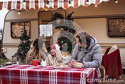 Family Christmas in camper: young mum, dad and kid drink hot cocoa outside Rv car decorated for Xmas Stock Photo