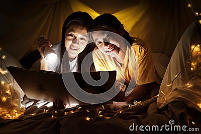 Family concept. Mother and child daughter reading book with flashlight together in children tent before bedtime. Happy mother read Stock Photo