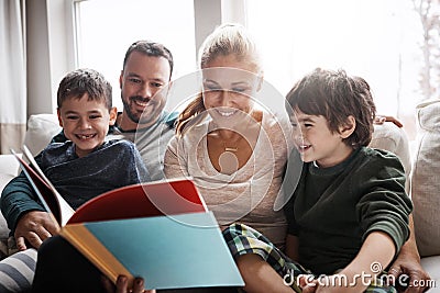 Family, couple and children on sofa for storytelling time with books and learning in family home. Love, reading and Stock Photo