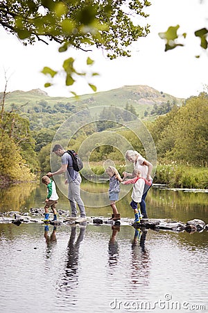 Family Crossing River Whilst Hiking In UK Lake District Stock Photo